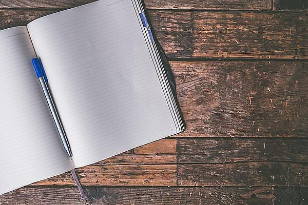 A blank open notebook on a table with a pen resting in the middle